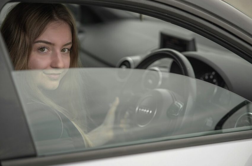 Devojka sedi u automobilu i drži volan