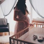 Trudna žena stoji pored bebinog kreveta u sobi