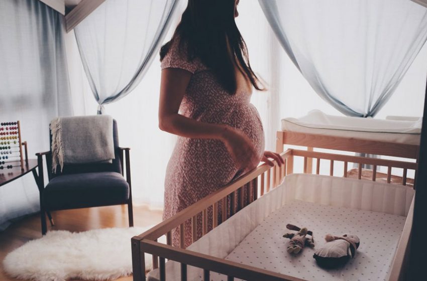 Trudna žena stoji pored bebinog kreveta u sobi